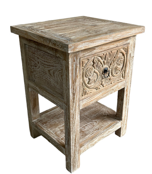 A Teak wood white washed bedside table with one drawer and bottom shelf, featuring floral patterns on the drawer front. Side view